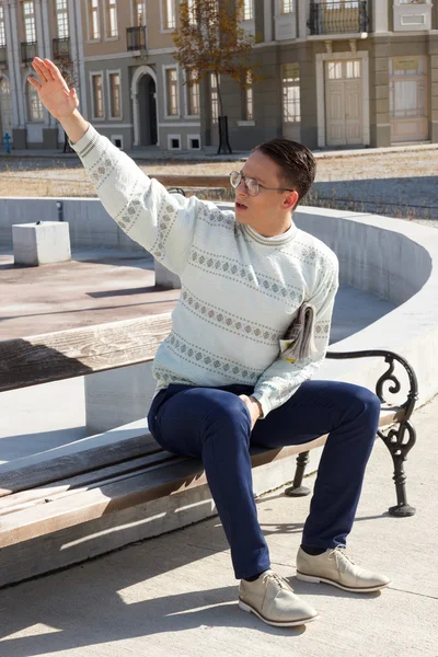 Mann mit Brille im weißen Pullover sitzt auf Bank und hält eine — Stockfoto