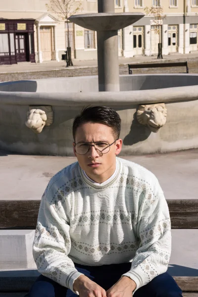 Mann mit Brille im weißen Pullover sitzt auf Bank neben Brunnen — Stockfoto