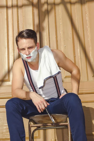 Homem com espuma de barbear em seu rosto e toalha em torno de seu pescoço siti — Fotografia de Stock