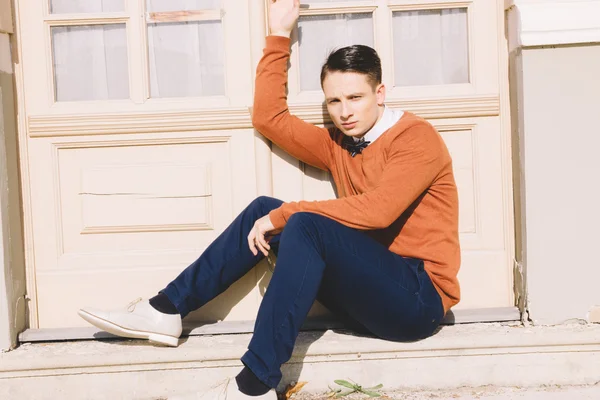 Young man in sweater sitting on steps in front of house and posi — Stock Photo, Image