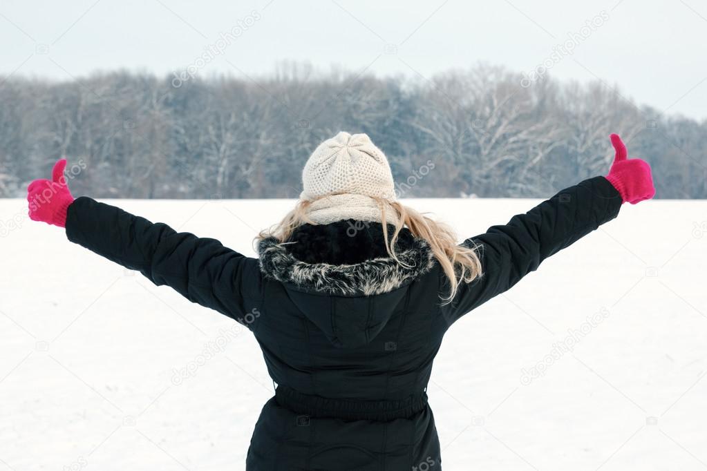 woman in snow showing her back and facing forest with thumbs up 