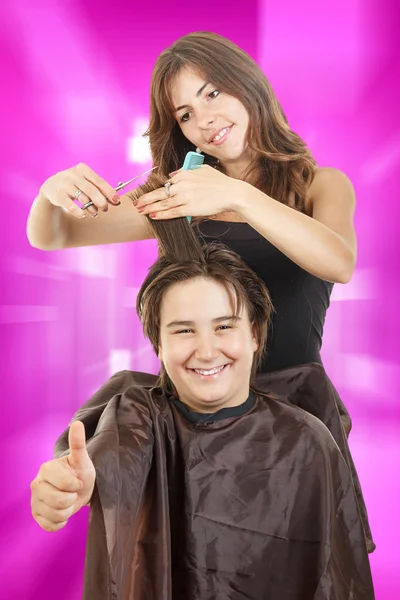 Pojke ler med långt hår med tumme upp mot glad kvinnliga hairdre — Stockfoto