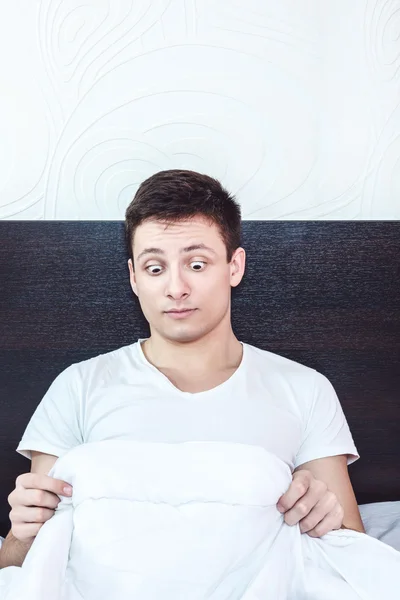 Przystojny młody mężczyzna w łóżku patrząc na jego penisa pod wh — Zdjęcie stockowe