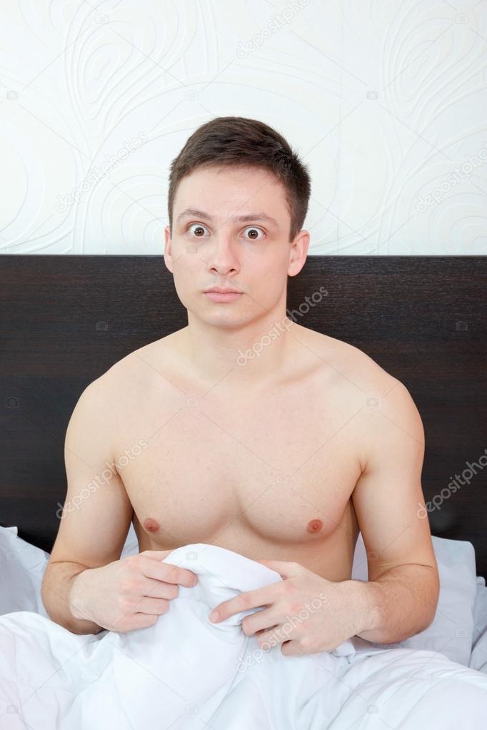 Shocked young impotent man hiding his penis under sheets