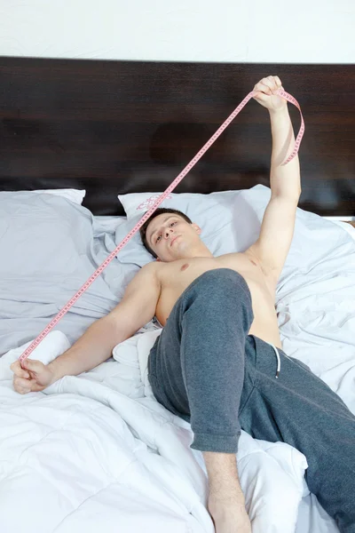 Młody przystojny mężczyzna pół nagie gospodarstwa centymetrem na łóżku — Zdjęcie stockowe