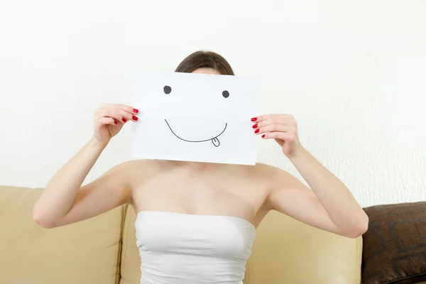 Girl cover her face with joyful teasing smile drawn on paper. — Stockfoto