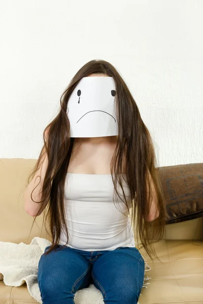 Adult girl cover her face with sad smile drawn on paper with one Stockbild