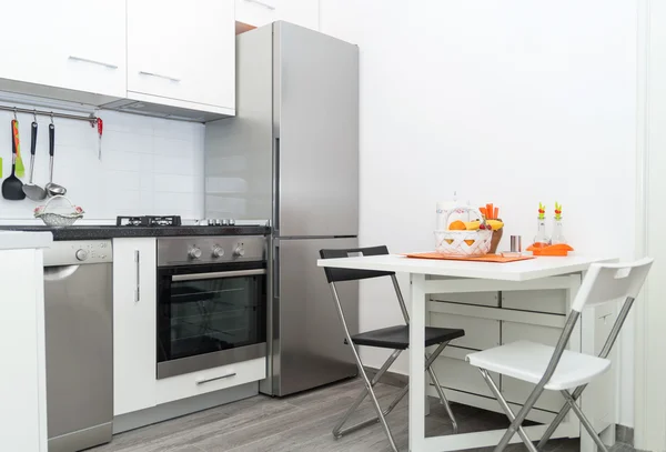 Cocina con cesta de fruta fresca en mesa blanca con dos sillas Imagen De Stock