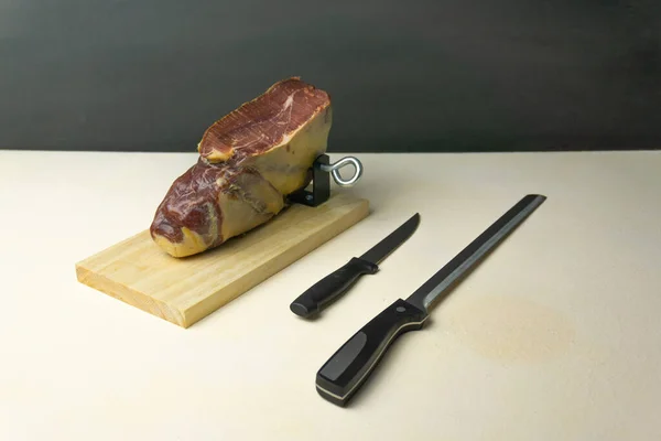 View of a boneless cured ham in a ham holder next to a knife and a knife sharpener