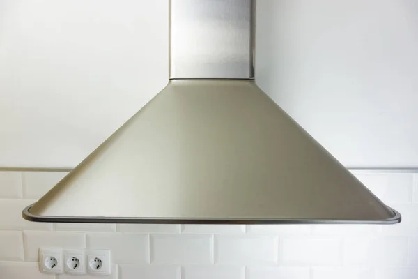 View of a stainless steel range hood in a white tiled kitchen with three european plugs