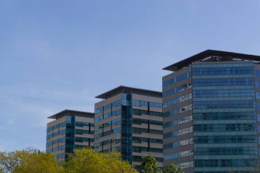 Geniş pencereli ve açık gökyüzü olan üç ofis binasının resmi