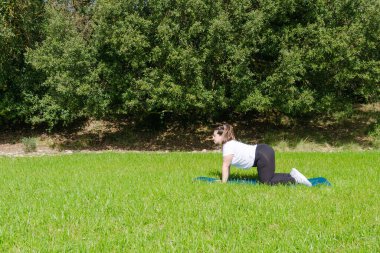 İnek pozuyla çimlerin üzerinde yoga yapan kıvrımlı kadın.