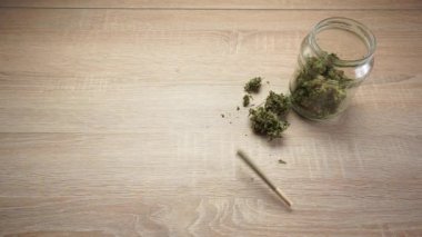 CBD eklem yeri ve yanında tomurcuklarla dolu cam bir kavanozla ahşap bir masanın üstüne düşen siyah çakmak.