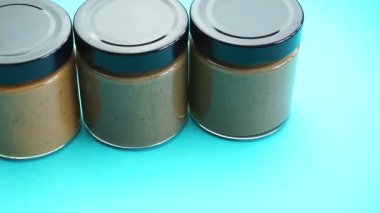 Siyah kapaklı cam kavanozlar, içinde kızarmış tahini, mavi bir arka planda, sağlıklı yiyecekler.