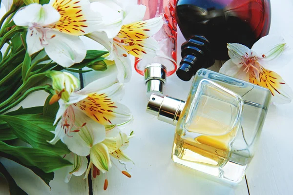 Flaschen mit Parfüm und aromatischen Ölen, umgeben von frischen Blumen — Stockfoto