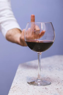 Bir adam orta parmağını bir bardak şaraba gösteriyor. Alkolden kaçınmak