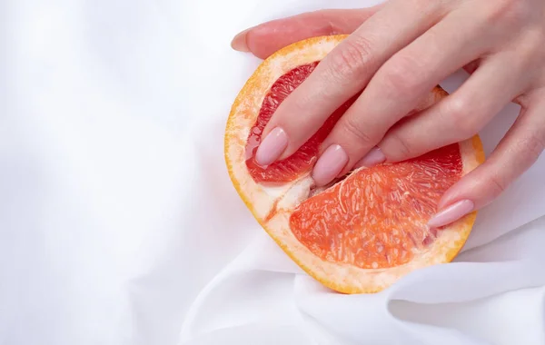 Güzel kadın parmakları ve greyfurt. Kadın cinselliğinin sembolü.