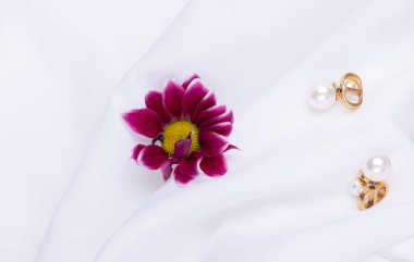 Beyaz arka planda kadın küpeleri ve çiçek.