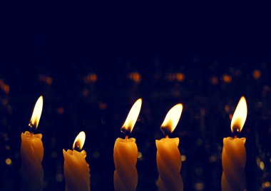 Several tall candles lit in a dark room