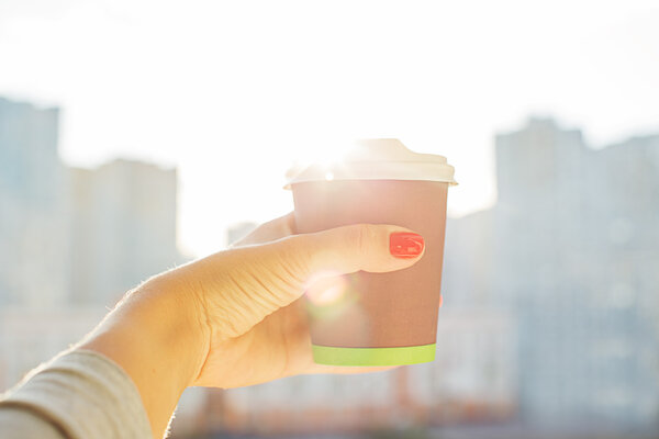 hand holding paper cup of coffee on natural morning background