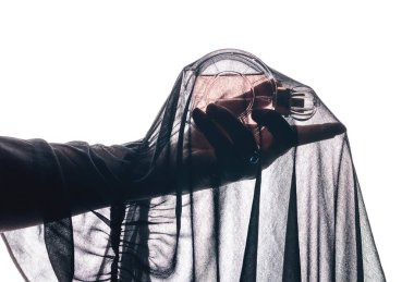 A woman's hand elegantly holds a glass perfume bottle on a pink background