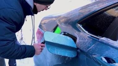 Bir adam arabasındaki buzları temizler..