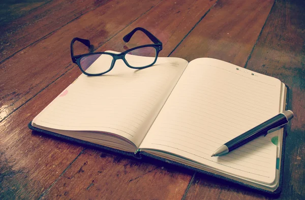 Prázdné notebook s brýlemi a pera na dřevěné pozadí — Stock fotografie