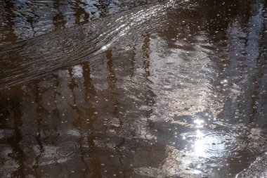 Parlak güneş parlıyor ve su birikintisinde küçük dalgalar oluşuyor. Bir soyutlama.