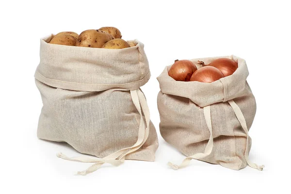 Soğan ve patates doğal keten torbalarda saklanır. Beyaz bir arkaplanda izole edilmiş.