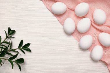 Pembe masa örtüsü üzerinde beyaz yumurtalar. Masa üstü dokusu. Yeşil yapraklar. Paskalya çizimi.