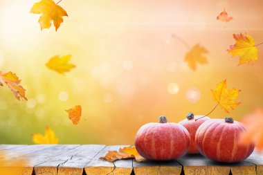 Ahşap bir masa ve renkli yapraklar üzerinde balkabaklarıyla sonbahar arkaplanı. Parlak güneş ışığı ve ılık mevsimsel atmosfer.