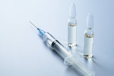 Işık arka planında temiz sıvıyla dolu iki cam ampullü tıbbi şırınga. Aşı, ilaç, sağlık ve tedavi kavramı.