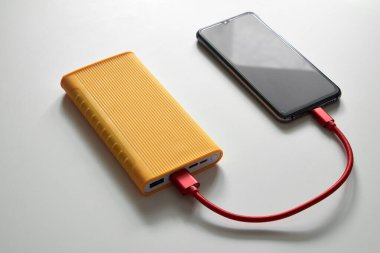 Beyaz arka planda sarı güç bankası ve kırmızı USB kablosu ile akıllı telefon şarjı, mobil cihazlar için taşınabilir pil, modern teknoloji ve enerji kavramı.