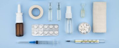 Mavi arka planda tıbbi malzemeler ve ilaçlar, haplar, şırıngalar, ampuller, termometre ve burun spreyi. Sağlık, tedavi ve eczane kavramı.