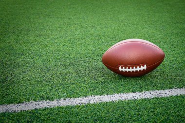Amerikan futbolu yeşil yapay çim üzerinde, beyaz bir çizginin yanında, fotokopi alanı olan açık alanda dinleniyor..