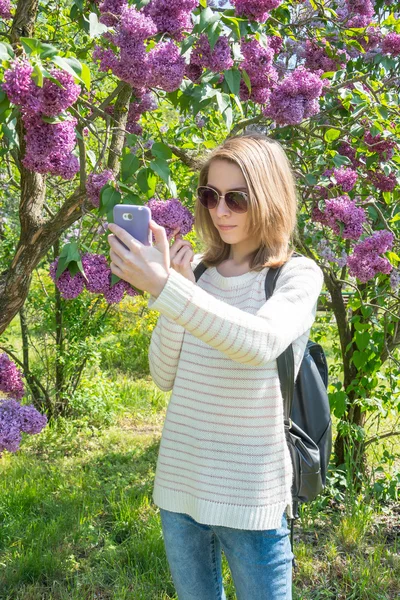 A rapariga fotografa lilás no telemóvel. Menina fazendo selfie — Fotografia de Stock