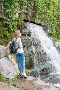 Kız bir parkta bir şelale yanında ayakta