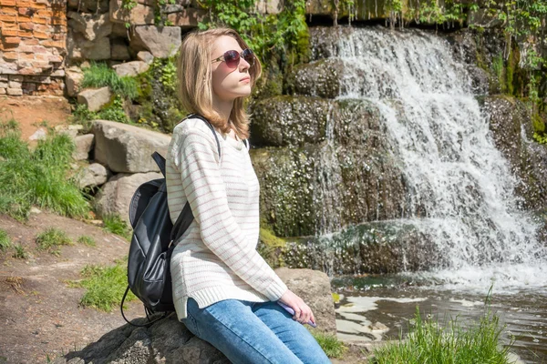 Mädchen sitzt in der Nähe eines Wasserfalls in einem Park — Stockfoto