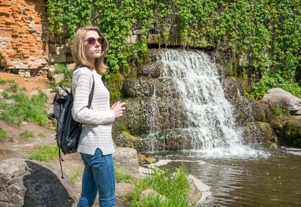 Flickan står nära ett vattenfall i en park — Stockfoto