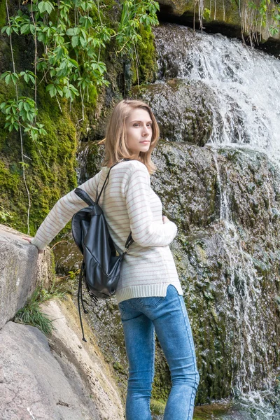 Flickan står nära ett vattenfall i en park — Stockfoto