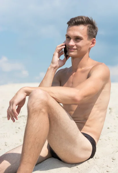 Jovem atlético com celular na praia — Fotografia de Stock