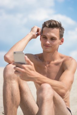 Sahilde cep telefonu ile genç atletik erkek