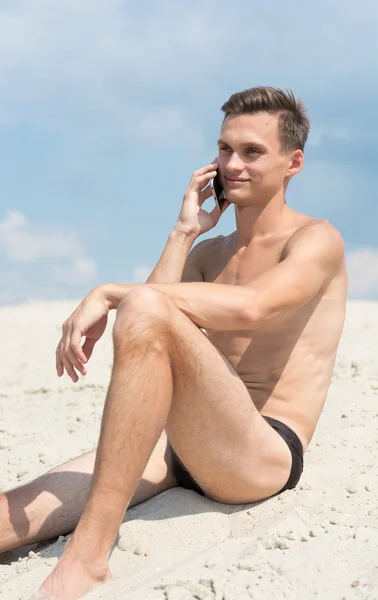 Jovem atlético com celular na praia — Fotografia de Stock