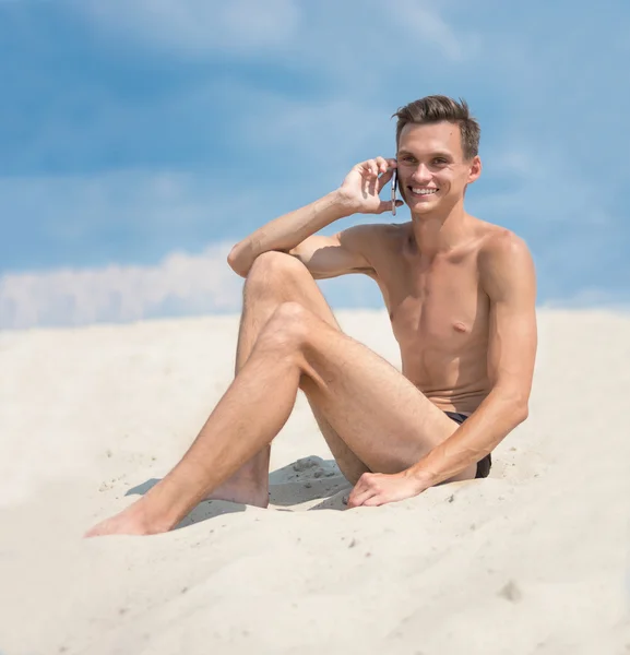 Young athletic tanned man with cellphone on the beach. — Stock Photo, Image