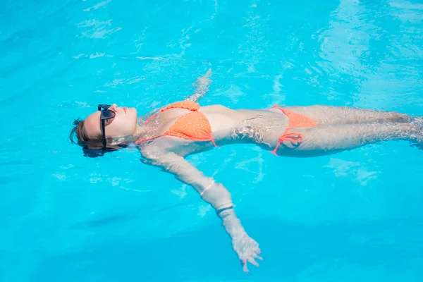 Mujer se relaja en una piscina en el traje de baño azul y gafas de sol . — Foto de Stock