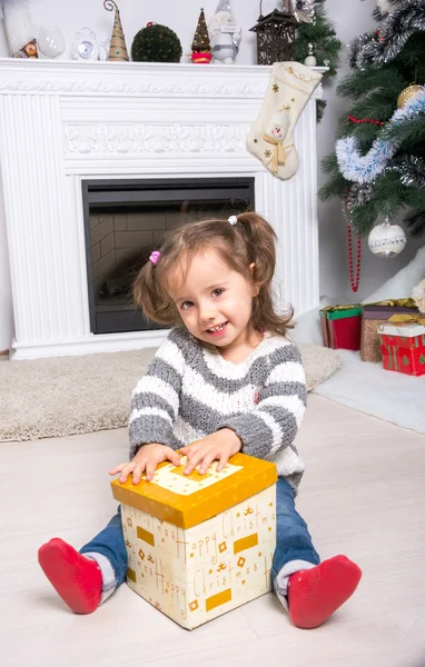 Kind unterm Weihnachtsbaum am Kamin öffnet Geschenk. — Stockfoto