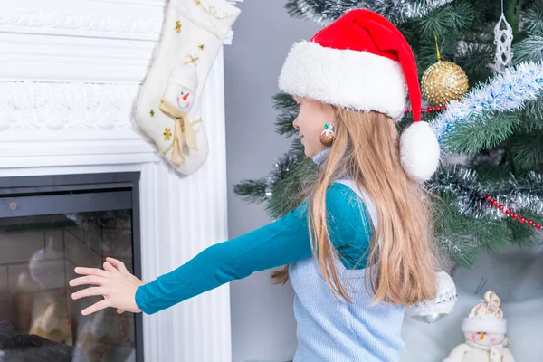 Girl in santa hat near the fireplace — Stock Photo, Image