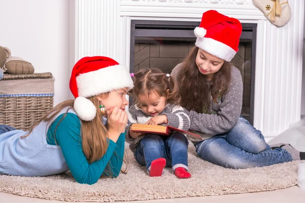 Ältere Schwestern lesen seiner kleinen Schwester eine Weihnachtsgeschichte vor. — Stockfoto