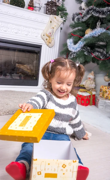 Child under the Christmas tree near the fireplace opens gift. — Stock Photo, Image