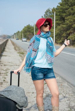 Yolda deniz kenarında bavulla genç kadın otostop